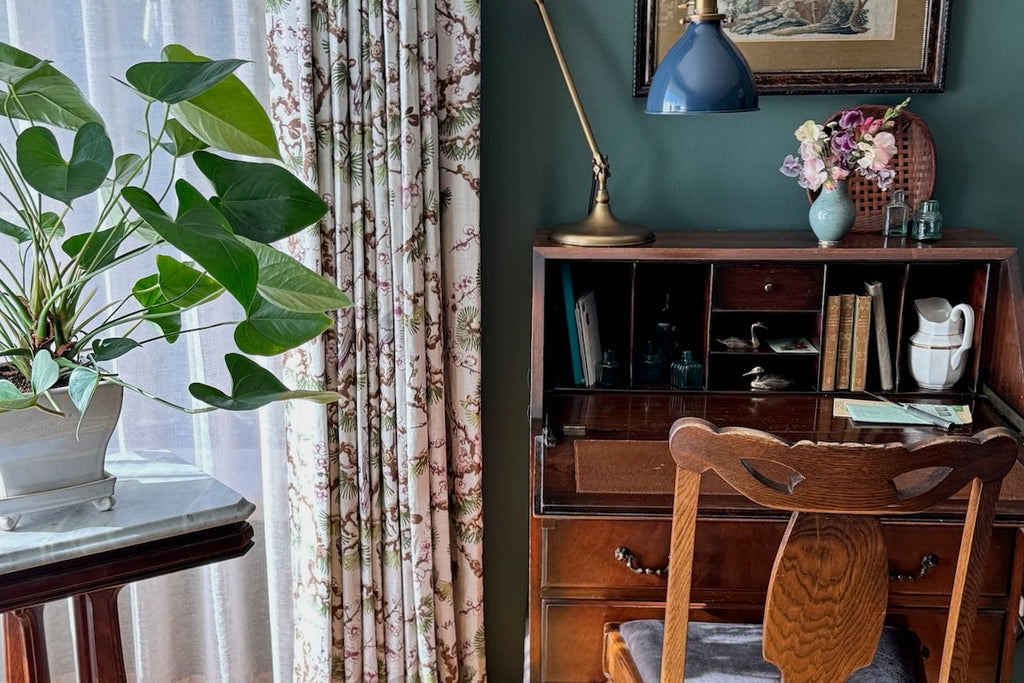 A secretary desk against a green wall with patterned drapery
