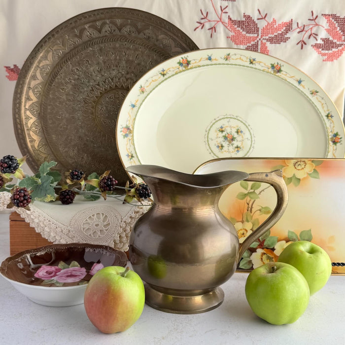 Arrangement of autumn colored items on a table - brass tray and pitcher, cream platters, green apples