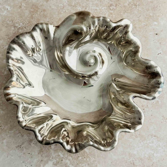 Overhead view of vintage silverplate footed bowl with ruffled undulating rim and raised spiral center, shot on neutral stone surface