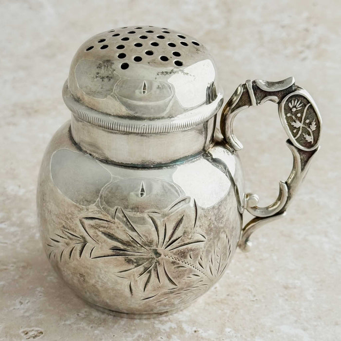 Silver shaker with decorative handle on a light background