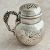 Silver shaker with intricate designs on a beige background