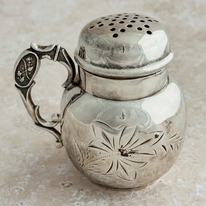 Silver shaker with intricate designs on a beige background