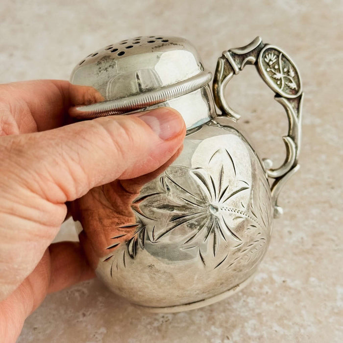 Hand holding a silver shaker with intricate designs