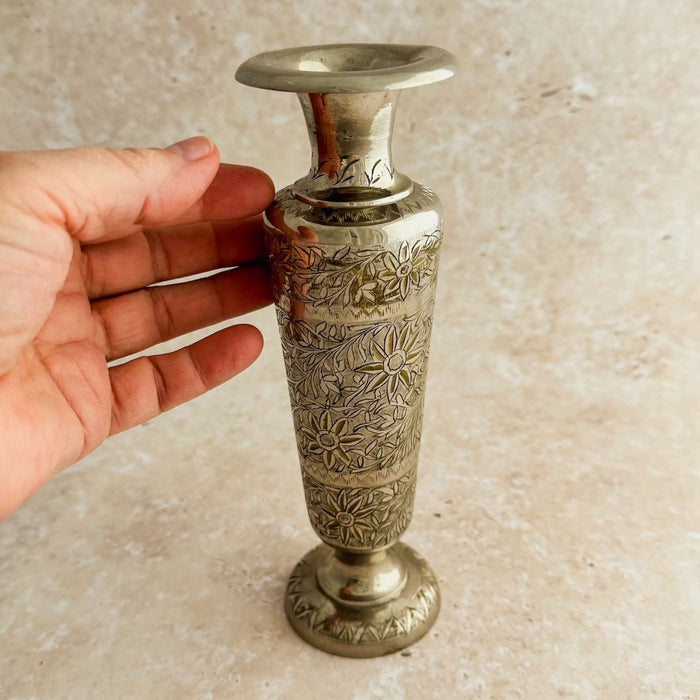 Hand holding a small silver vase with intricate designs