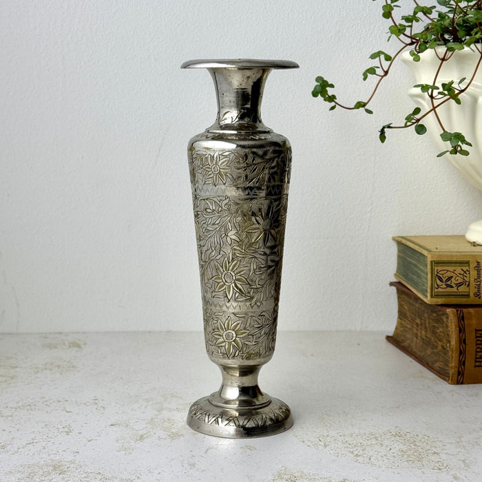 Vintage silver-colored brass bud vase with engraved floral decoration, narrow flared neck, and round footed base.