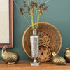 Silver-colored engraved brass bud vase holding tall dried stems, styled with woven baskets and brass quail figurines.