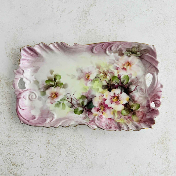 Vintage hand-painted porcelain tray with wild rose spray in cream and blush, scrolled mauve and lavender embossed border, and gold rim, viewed from above
