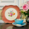 Styled view of cake plate standing upright behind a teacup and saucer on a kitchen counter