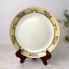 Antique hand painted porcelain plate with yellow border, pink flowers, and green geometric decoration shown on a plate stand