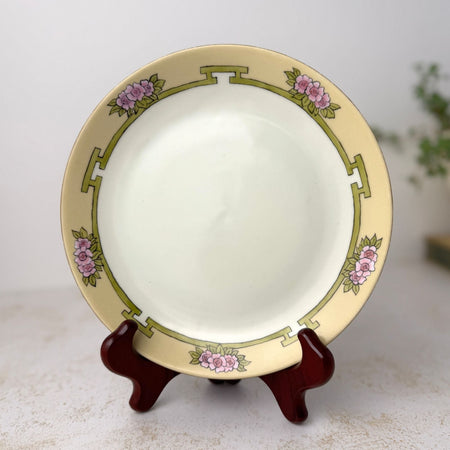 Antique hand painted porcelain plate with yellow border, pink flowers, and green geometric decoration shown on a plate stand