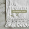 Close-up of one white pillowcase showing the side seam shifted inward above the crochet lace edge with an arrow and condition note