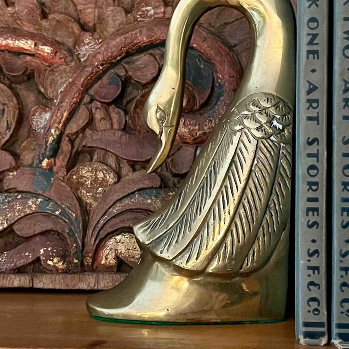 Styled shot of swan bookend with books against carved wood panel
