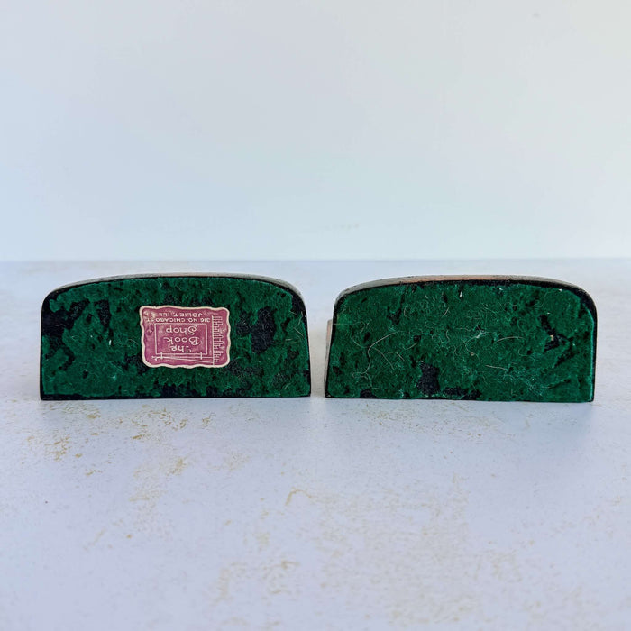 Undersides of vintage cast iron duck bookends showing worn green felt and retailer sticker reading "The Book Shop, 316 No. Chicago St., Joliet, ILL"