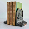 Vintage cast iron bookends in use with leather-bound books, showing duck-in-flight relief panel with dark finish and copper highlights