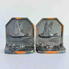 Pair of vintage cast iron bookends facing forward, each showing relief panel of a duck in low flight over water, dark finish with copper-toned highlights