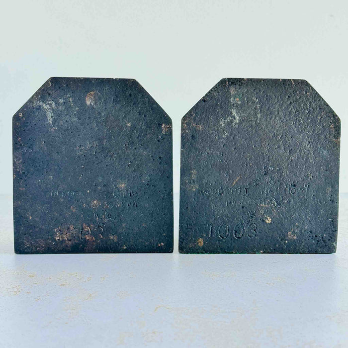 Backs of vintage cast iron duck bookends showing textured iron surface and partially legible stamped maker's mark and model number 1003