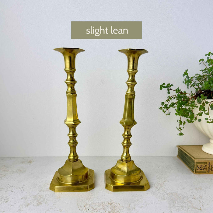 Two matching brass candlestick holders showing a slight lean in one candlestick, with a text label reading 'slight lean'
