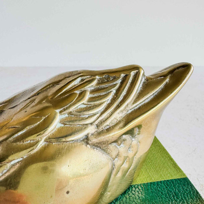 Close-up of brass duck wing showing raised feather design, patina, and vintage surface wear