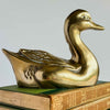 Vintage brass duck figurine displayed on a book, showing warm brass finish and decorative bird shape