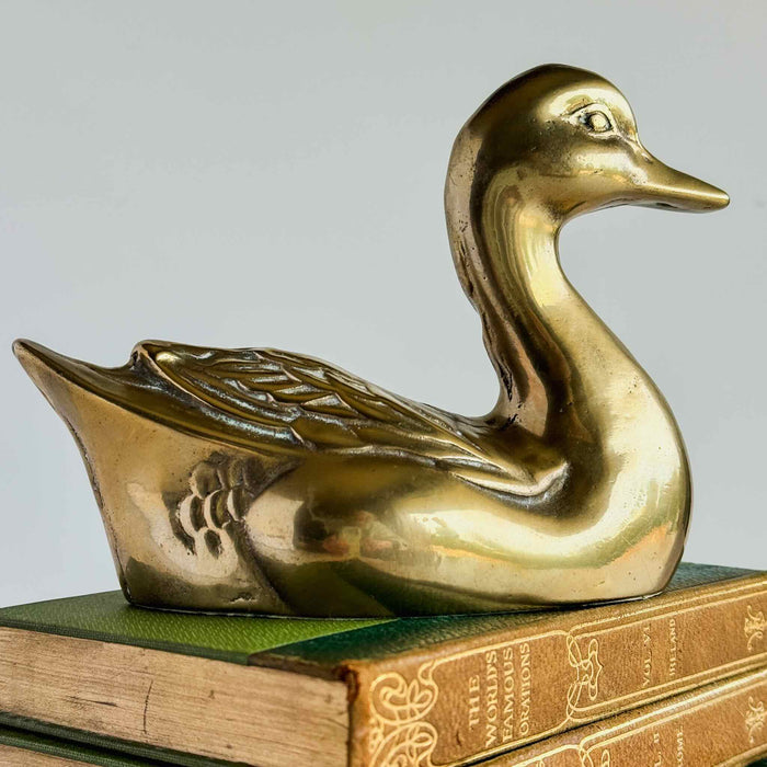 Vintage brass duck figurine displayed on a book, showing warm brass finish and decorative bird shape