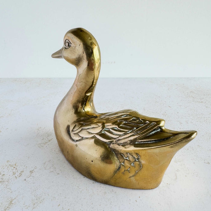 Second side view of brass duck figurine showing raised feather pattern and aged brass surface