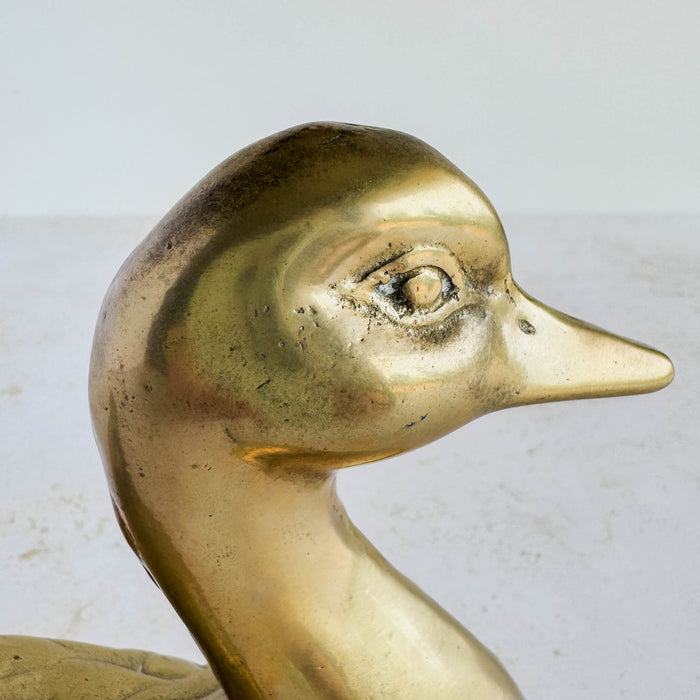 Close-up of duck figurine head showing stylized face, eye detail, and vintage brass patina