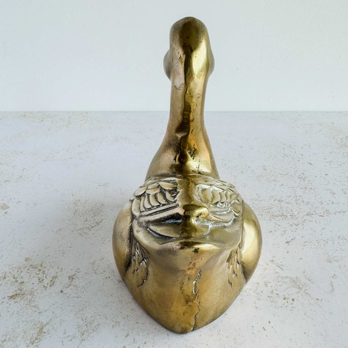 Back view of vintage brass duck figurine showing narrow profile, head shape, and wing detailing