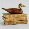Wood and brass duck figurine on a stack of books against a light background