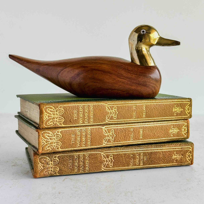 Wood and brass duck figurine on a stack of books against a light background