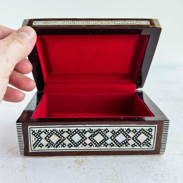 Inlaid wood box with a hand lifting the lid showing red interior