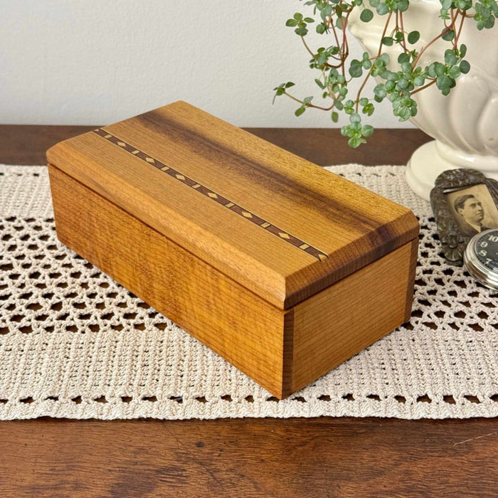Vintage inlaid wood box with warm grain, striped lid detail, and chamfered corners, styled on a crochet runner with trailing plant, and keepsake items