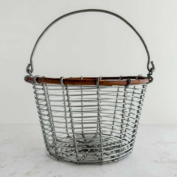 Front view of wire and twig basket with handle raised against a light background