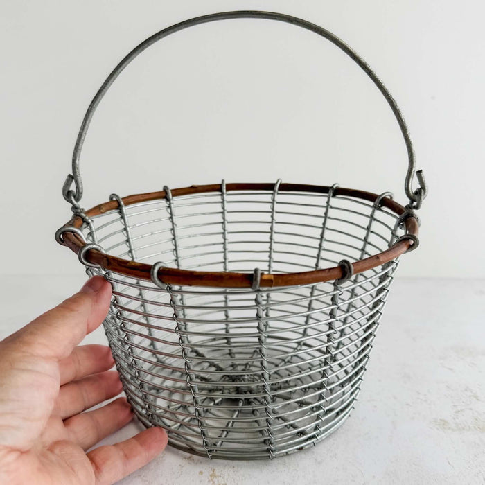 Wire and twig basket with handle up and hand touching side of basket