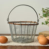 Vintage round wire egg gathering basket with raised handle, natural twig rim detail, and soft metallic gray finish, styled with brown eggs on a crochet runner