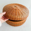 Hand holding a woven basket with a lid on a light background
