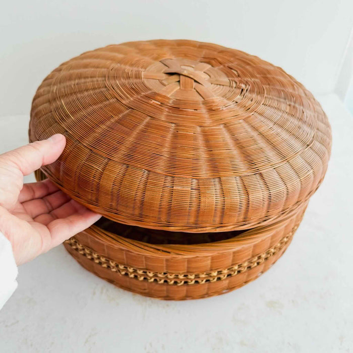 Hand holding a woven basket with a lid on a light background