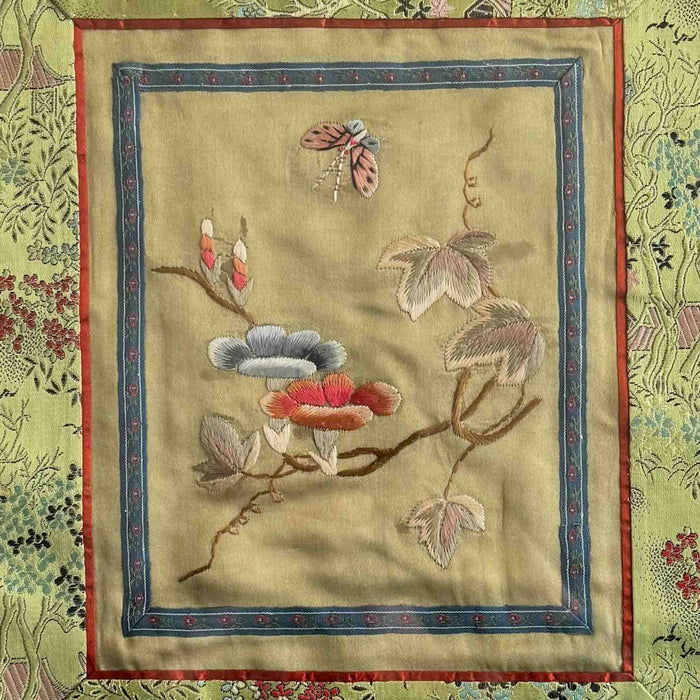 Close-up of embroidered panel with floral and leaf design on a pale gold fabric 