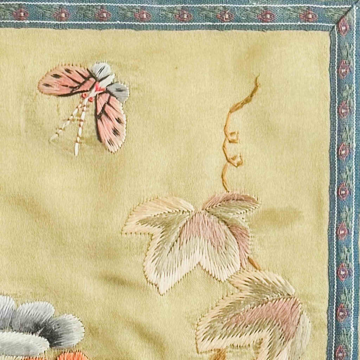 Close-up of embroidered butterfly and vine leaves on a pale gold background