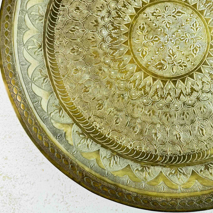 Close-up of the hand-tooled floral and geometric pattern in the lower-left section of the brass tray