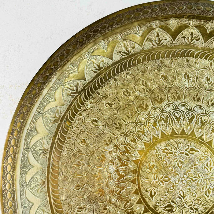 Close-up of the hand-tooled floral and geometric pattern in the upper-left section of the brass tray