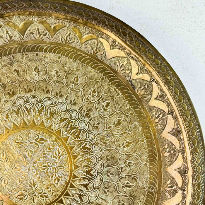 Close-up of the hand-tooled floral and geometric pattern in the upper-right section of the brass tray