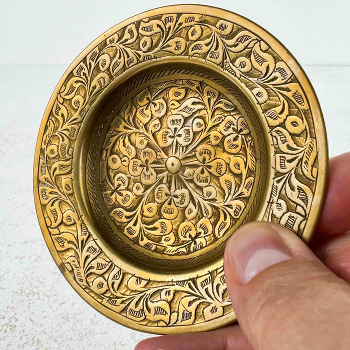 Close-up of second vintage brass trinket dish held in hand, showing variation in hand-engraved floral and foliate pattern compared to companion dish