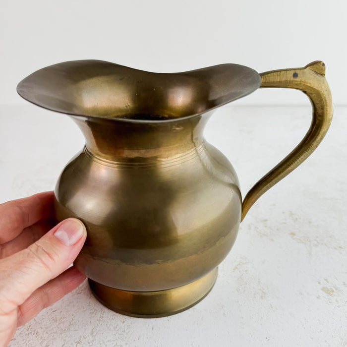 Slightly angled view of vintage brass pitcher with hand for scale