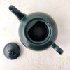 Overhead view inside the matte black teapot with the lid removed and placed alongside