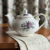 Vintage Royal Grafton English bone china purple violets teapot on antique table with linen tea towel and blurred floral drapery in background