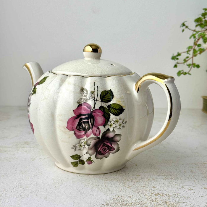 Vintage Gibsons Staffordshire England teapot, three-quarter view showing pink and black roses, gold-trimmed handle, and crazed ivory glaze.