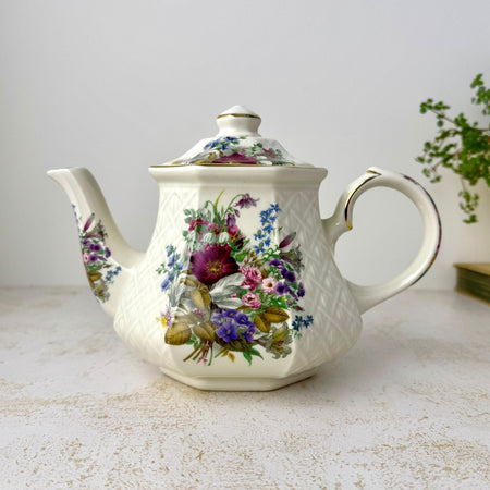 Front view of vintage Sadler Windsor teapot with multicolor floral decoration, embossed basket-weave sides, and gold trim styled with trailing plant