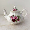 Heirloom fine bone china teapot with swirl-ribbed white body, sprays of pink and deep burgundy roses with green foliage, and gold trim at lid, base, and spout tip
