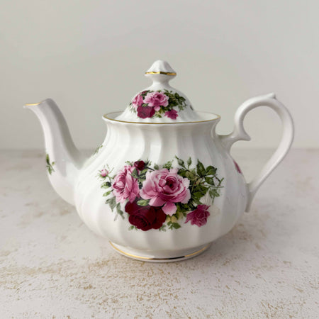 Heirloom fine bone china teapot with swirl-ribbed white body, sprays of pink and deep burgundy roses with green foliage, and gold trim at lid, base, and spout tip