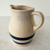 Side view of vintage beige stoneware pitcher showing rounded body, cobalt blue bands, spout, and handle